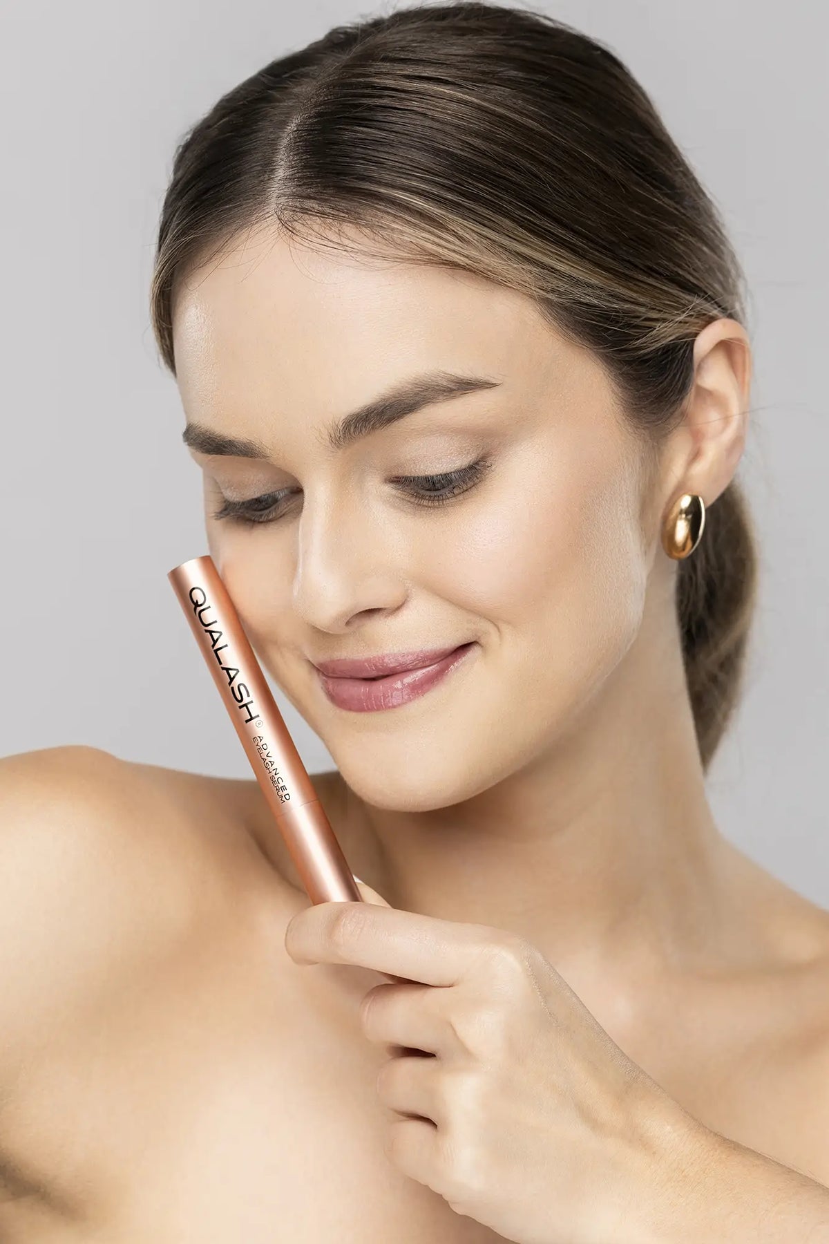 Sminkelő nő, aki QUALASH Advanced Eyelash Serumot tart